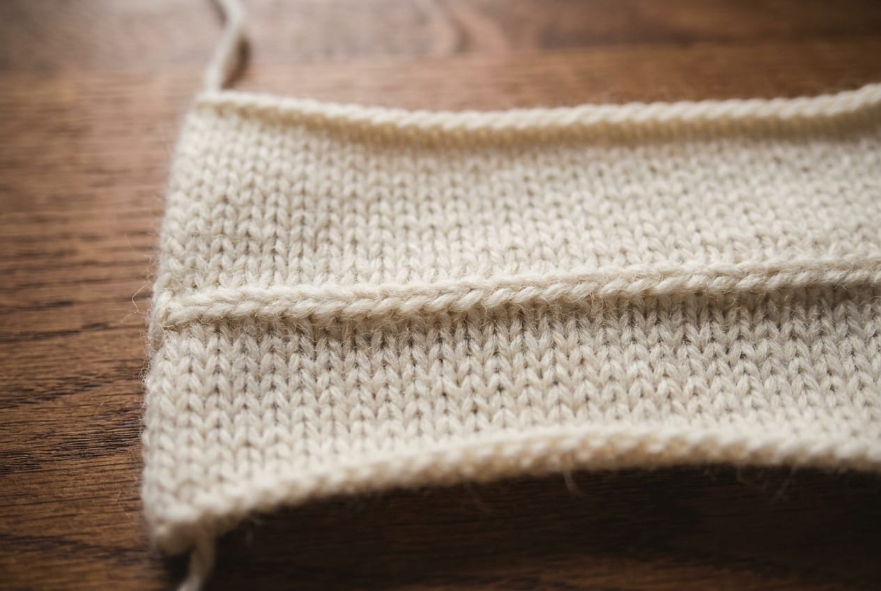 A finished invisible graft across a cream knitted piece, the join nearly impossible to see among the stitches.